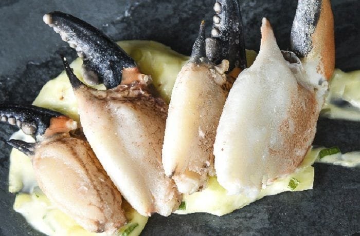 Cooked and cracked Chilean crab claws, served with scallion mayonnaise and lime as a seafood appetizer.