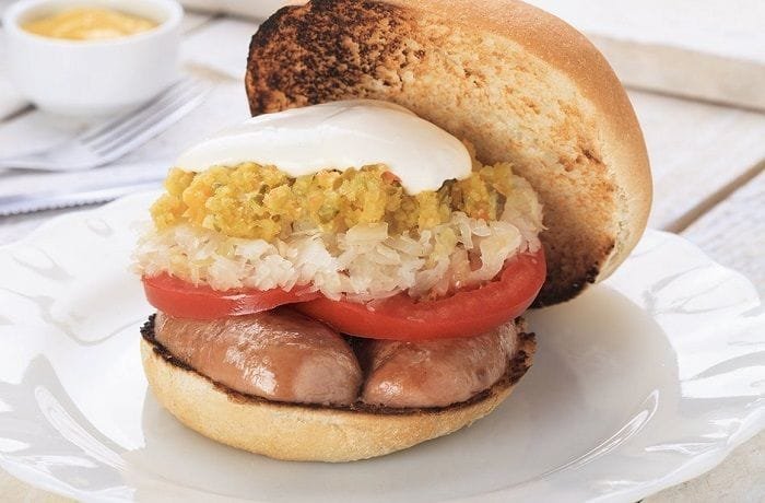 Open Chilean gorda completa sandwich with a thick split sausage, sauerkraut, tomato, and mayonnaise