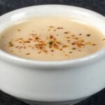 A bowl of creamy acevichada sauce, sprinkled with togarashi and served with lime and cilantro.