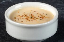 A bowl of creamy acevichada sauce, sprinkled with togarashi and served with lime and cilantro.