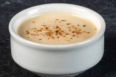 A bowl of creamy acevichada sauce, sprinkled with togarashi and served with lime and cilantro.