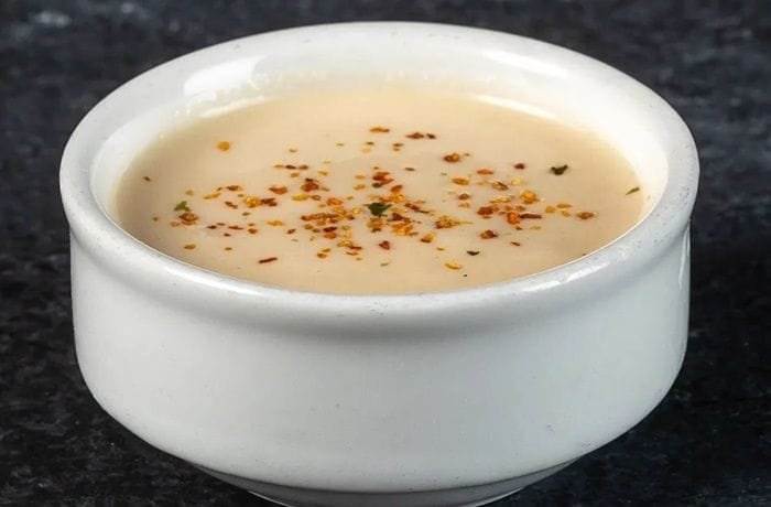 A bowl of creamy acevichada sauce, sprinkled with togarashi and served with lime and cilantro.