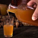 Amber homemade quince liqueur in a glass bottle and small glass next to fresh quinces