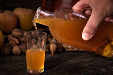Amber homemade quince liqueur in a glass bottle and small glass next to fresh quinces