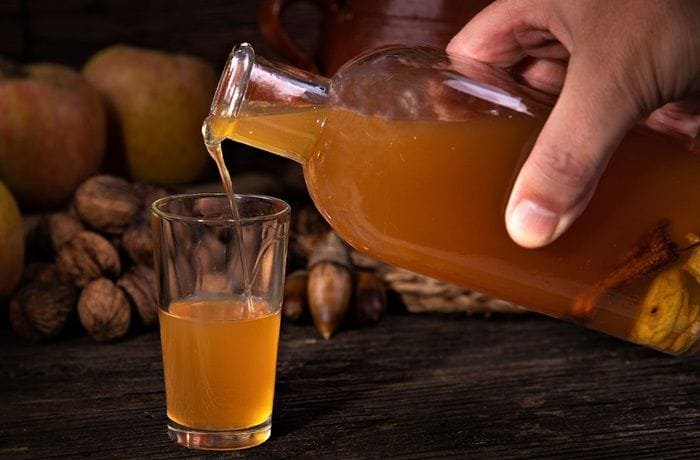 Amber homemade quince liqueur in a glass bottle and small glass next to fresh quinces