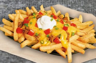 A generous plate of french fries topped with ground beef, melted cheddar cheese sauce, fresh diced tomato, chopped chives, and a touch of plain yogurt.