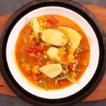 Hot Chilean locro falso with potatoes, squash, and corn in a deep clay bowl