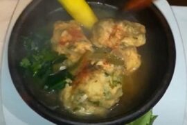 Hot Chilean machos ahogados soup in a clay bowl, with flour and egg dumplings floating in the broth