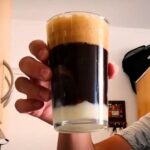 Chilean malta con licor de cacao cocktail served in tall glasses with a condensed milk layer, ice, and a dusting of cocoa.