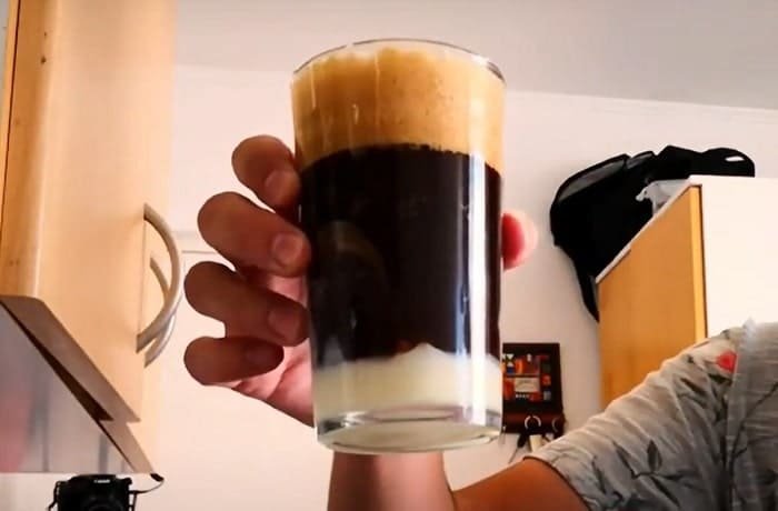 Chilean malta con licor de cacao cocktail served in tall glasses with a condensed milk layer, ice, and a dusting of cocoa.