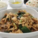 A glossy plate of Mongolian chicken served next to a mound of Chilean-style fried rice, topped with sliced scallions.