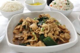 A glossy plate of Mongolian chicken served next to a mound of Chilean-style fried rice, topped with sliced scallions.