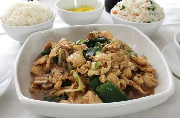 A glossy plate of Mongolian chicken served next to a mound of Chilean-style fried rice, topped with sliced scallions.