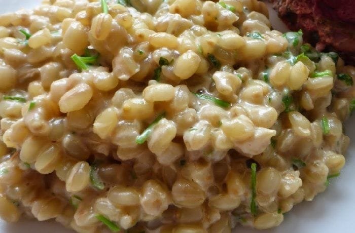 A plate of creamy mote risotto topped with Parmesan cheese, served in a deep dish.