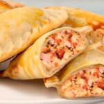A tray of golden, glossy Chilean Neapolitan empanadas with visible melted cheese, ham, and tomato filling.