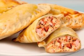 A tray of golden, glossy Chilean Neapolitan empanadas with visible melted cheese, ham, and tomato filling.