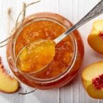 Amber-colored homemade Chilean peach jam in a glass jar with visible fruit pieces