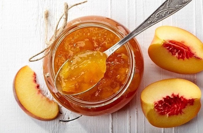 Amber-colored homemade Chilean peach jam in a glass jar with visible fruit pieces