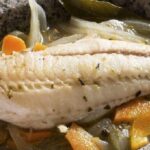 Chilean pescado en escabeche served cold in a glass dish with onion, carrot, and vinegar marinade