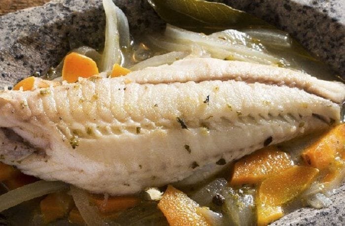 Chilean pescado en escabeche served cold in a glass dish with onion, carrot, and vinegar marinade
