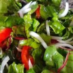 Fresh raw Swiss chard salad with tomato and red onion in a wooden bowl