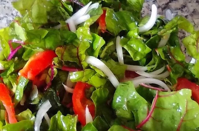 Fresh raw Swiss chard salad with tomato and red onion in a wooden bowl