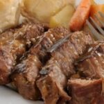 A large piece of oven-roasted Chilean plateada beef, golden and glossy, served in a dish with plenty of cooking juices and vegetables.