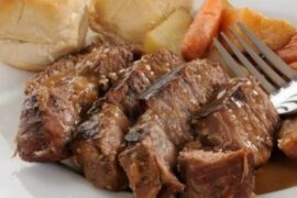 A large piece of oven-roasted Chilean plateada beef, golden and glossy, served in a dish with plenty of cooking juices and vegetables.
