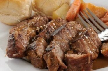 A large piece of oven-roasted Chilean plateada beef, golden and glossy, served in a dish with plenty of cooking juices and vegetables.