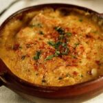 Clay bowl of Chilean seafood chupe, freshly baked with golden cheese and fresh parsley