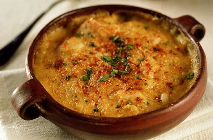 Clay bowl of Chilean seafood chupe, freshly baked with golden cheese and fresh parsley