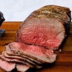 Thin slices of homemade roast beef, pink in the center, served on a wooden board with fresh herbs