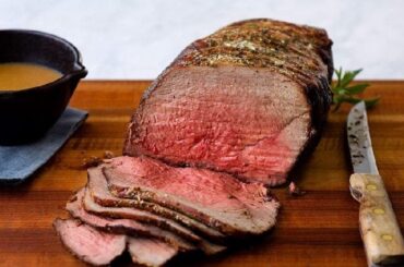 Thin slices of homemade roast beef, pink in the center, served on a wooden board with fresh herbs
