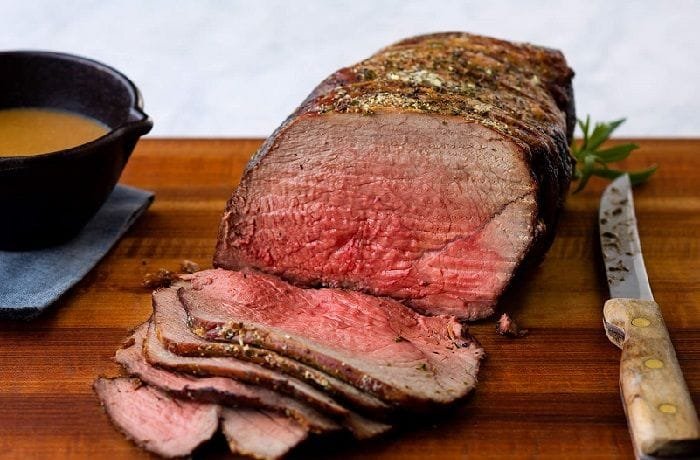 Thin slices of homemade roast beef, pink in the center, served on a wooden board with fresh herbs