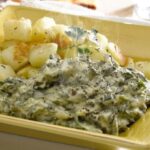 Dish of creamy Chilean Swiss chard stew with bright green leaves in a white sauce and melted cheese on top