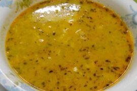 Steaming bowl of Chilean toasted flour soup with threads of egg white and a dusting of red merken on the surface