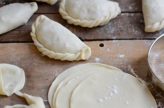 Assembling and sealing empanada dough discs filled with mushroom pino.