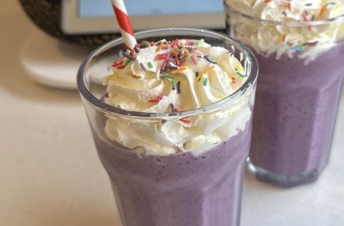 Homemade purple berry milkshake inspired by the Grimace Shake, topped with whipped cream