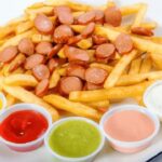 Homemade salchipapas, French fries and sliced fried sausages on a plate with sauces on the side