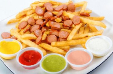Homemade salchipapas, French fries and sliced fried sausages on a plate with sauces on the side