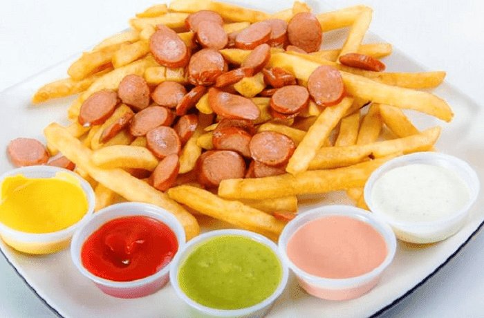 Homemade salchipapas, French fries and sliced fried sausages on a plate with sauces on the side