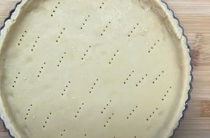 Kuchen dough pressed into a round baking tin, spread higher at the edges to hold the filling
