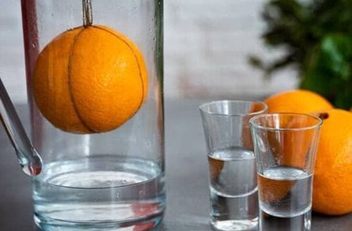 Organic orange hanging inside a jar above vodka
