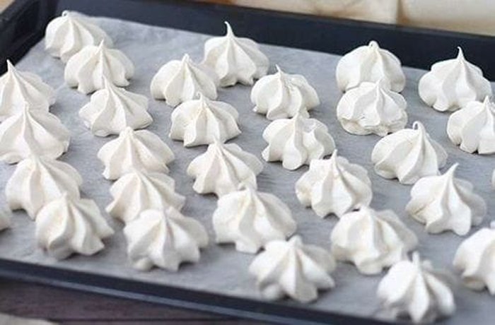 Piped merenguitos on a lined baking tray