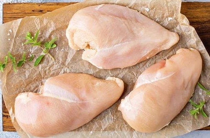 Clean, pink chicken breast fillets on a cutting board, ready to be cut into bite-sized pieces.
