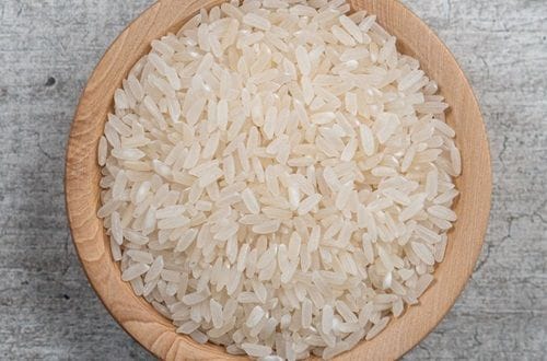 Raw white rice grain on a wooden board, ready to be sauteed.