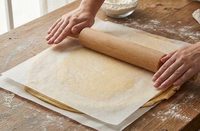 Chumbeque dough between two sheets of parchment paper being rolled out to 3 mm thick.