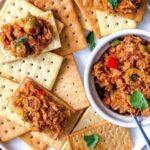 Tuna antipasto served in a bowl with stuffed olives and vegetables, with soda crackers on the side