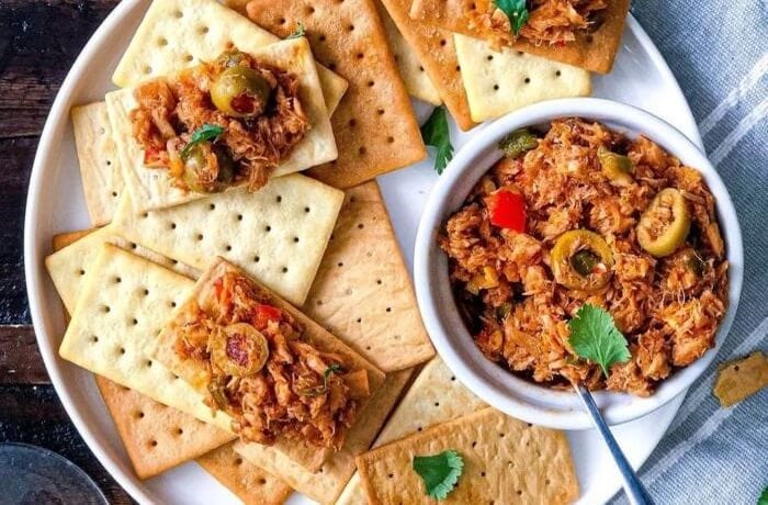 Tuna antipasto served in a bowl with stuffed olives and vegetables, with soda crackers on the side