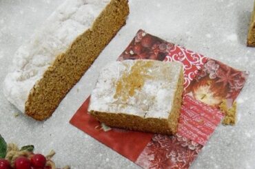 Rectangular Chilean honey bread dusted with powdered sugar, showing a dark spongy crumb, next to a cup of coffee